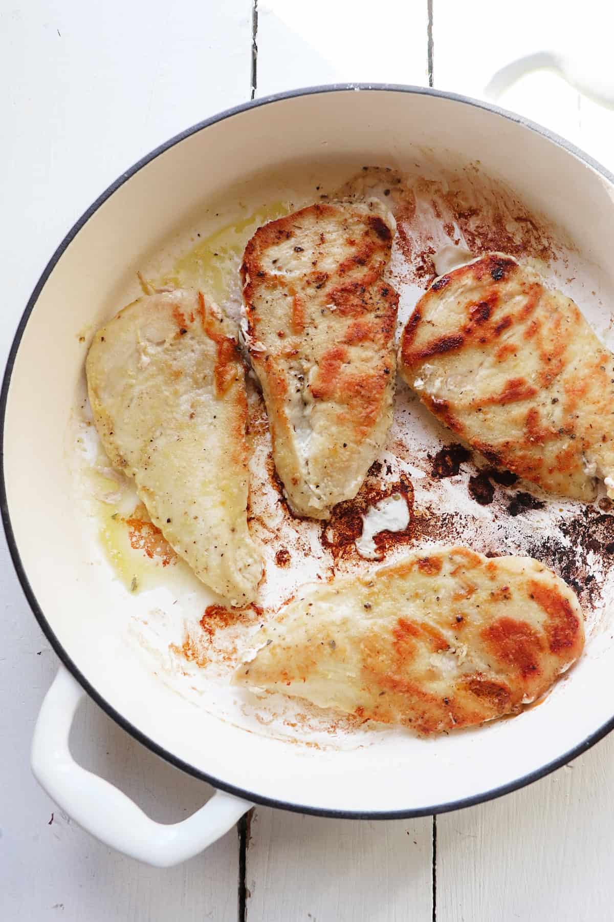 four browned chicken breasts in a white skillet.
