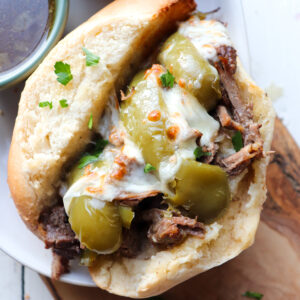 up close of finished slow cooker italian beef sandwich on a wooden board.