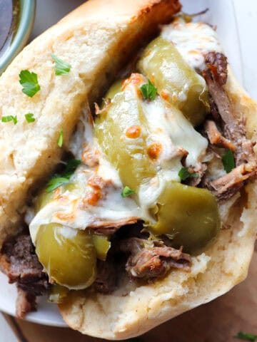 up close of finished slow cooker italian beef sandwich on a wooden board.