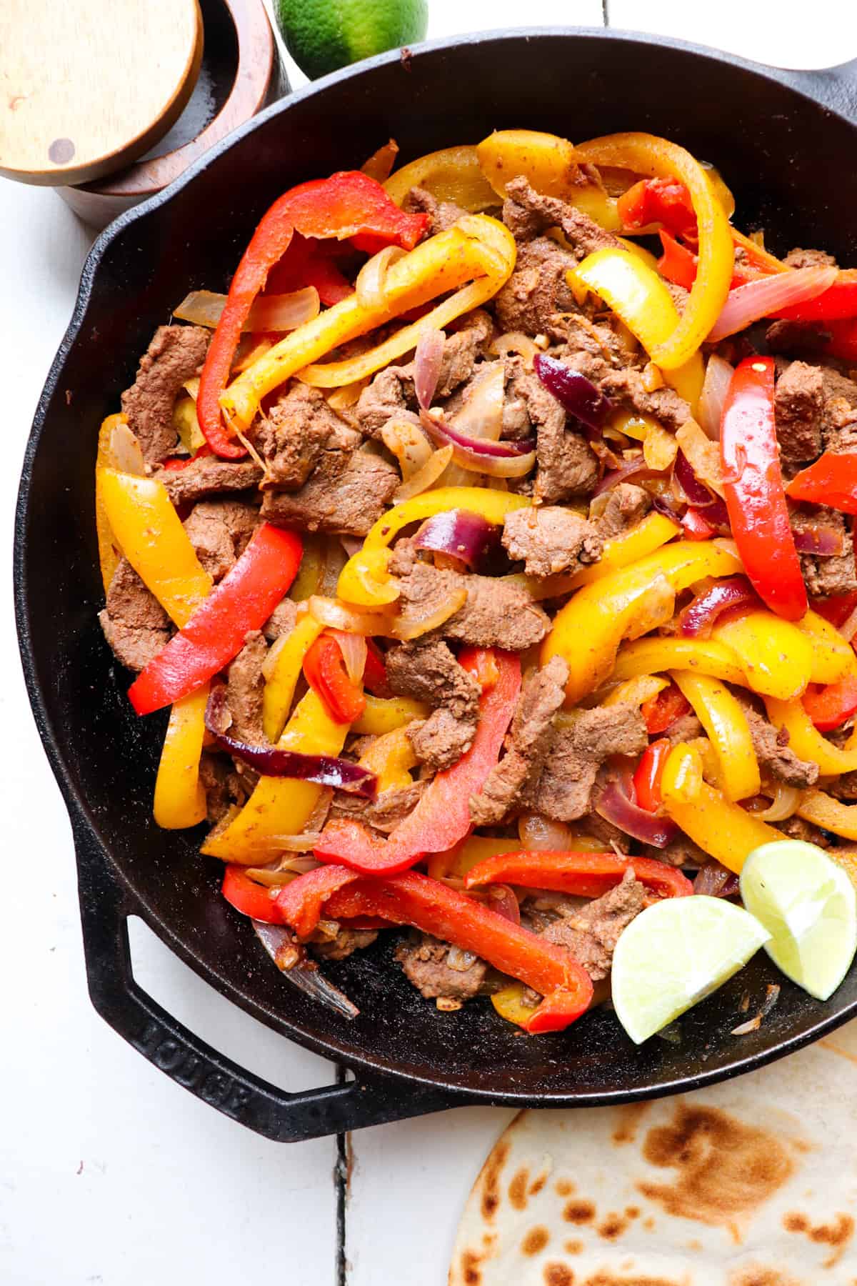 cast iron skillet filled with venison fajitas with tortillas and lime on the side.