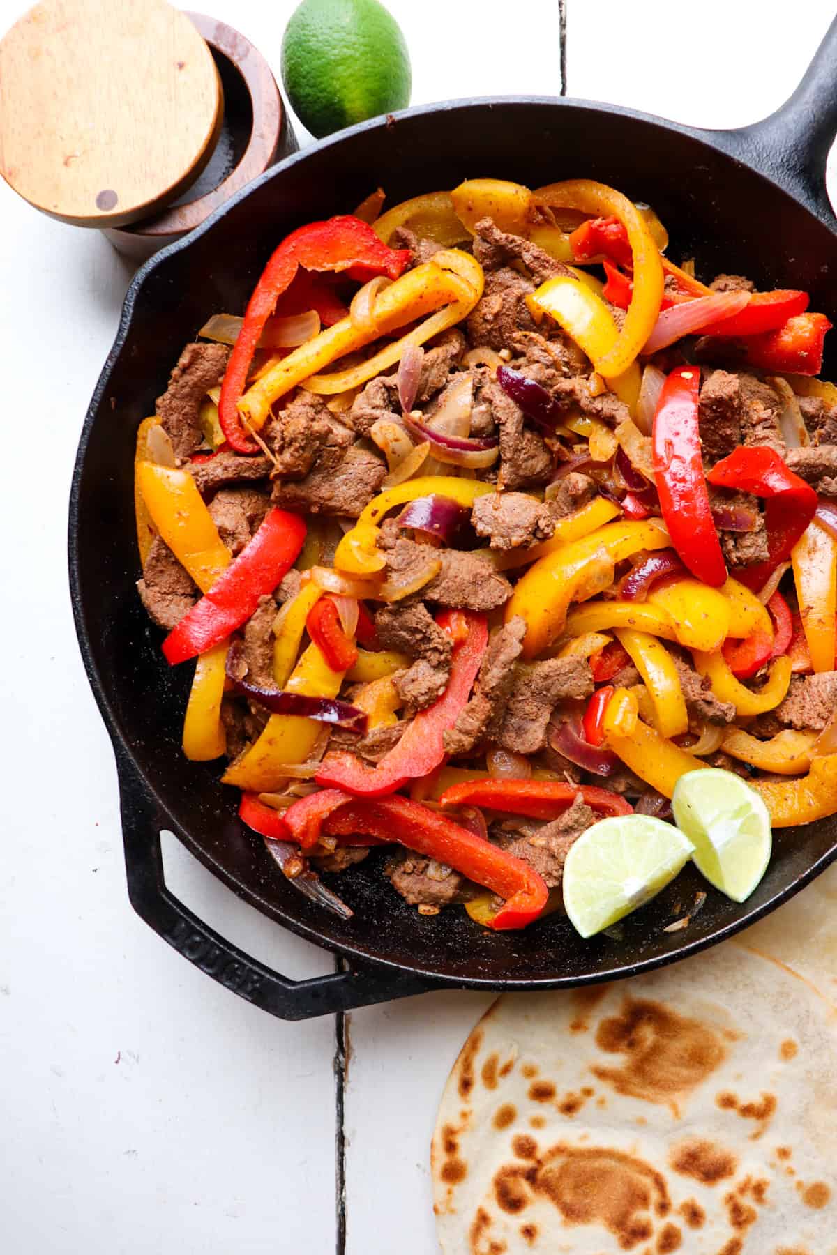 cast iron skillet filled with venison fajitas with tortillas and lime on the side.