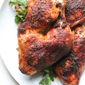 white platter with juicy baked chicken leg quarters on top garnished with parsley.