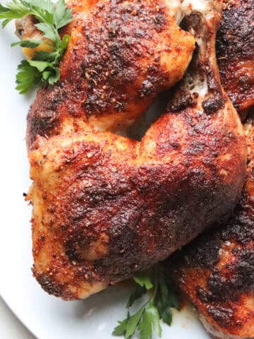 white platter with juicy baked chicken leg quarters on top garnished with parsley.