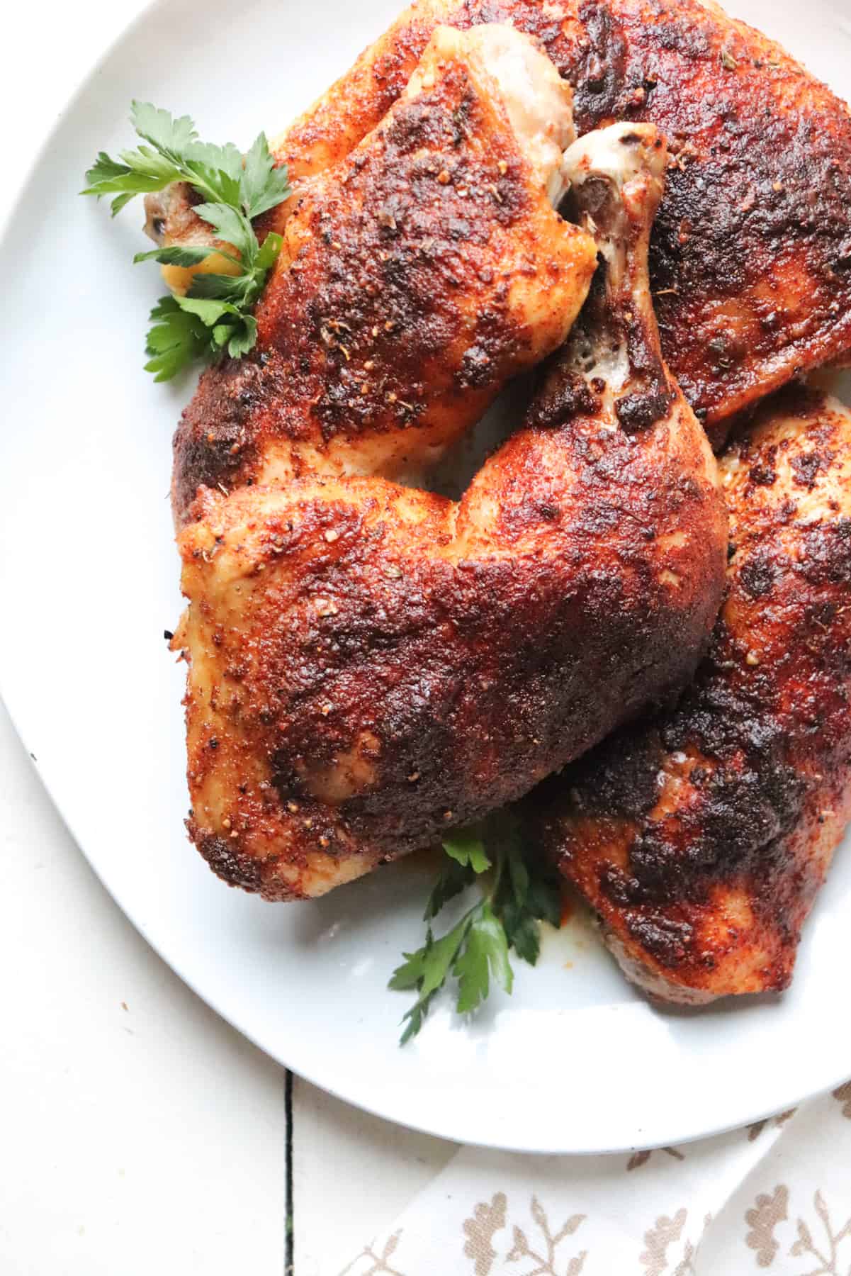 white platter with baked chicken leg quarters on top garnished with parsley.