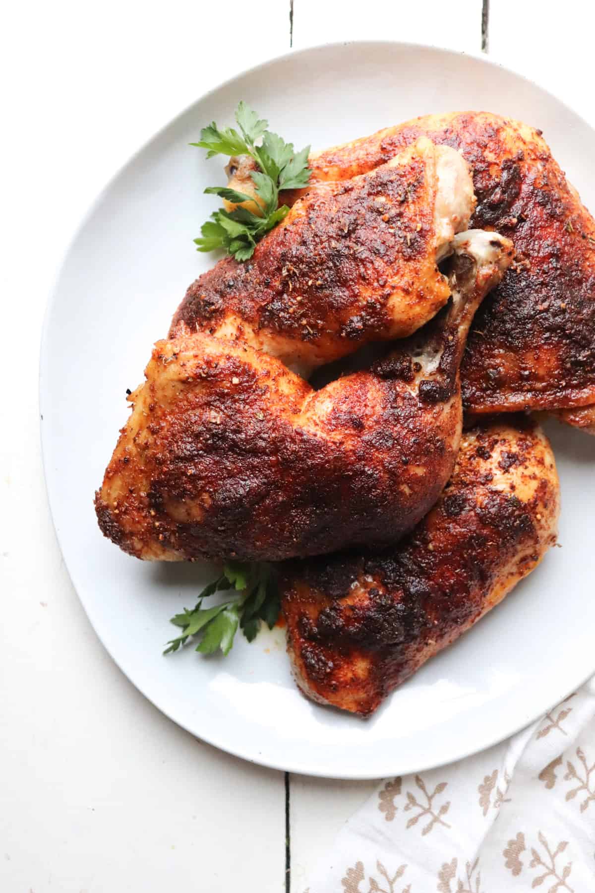 white platter with chicken leg quarters on top garnished with parsley.