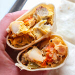 hand holding breakfast burrito with potoatoes.