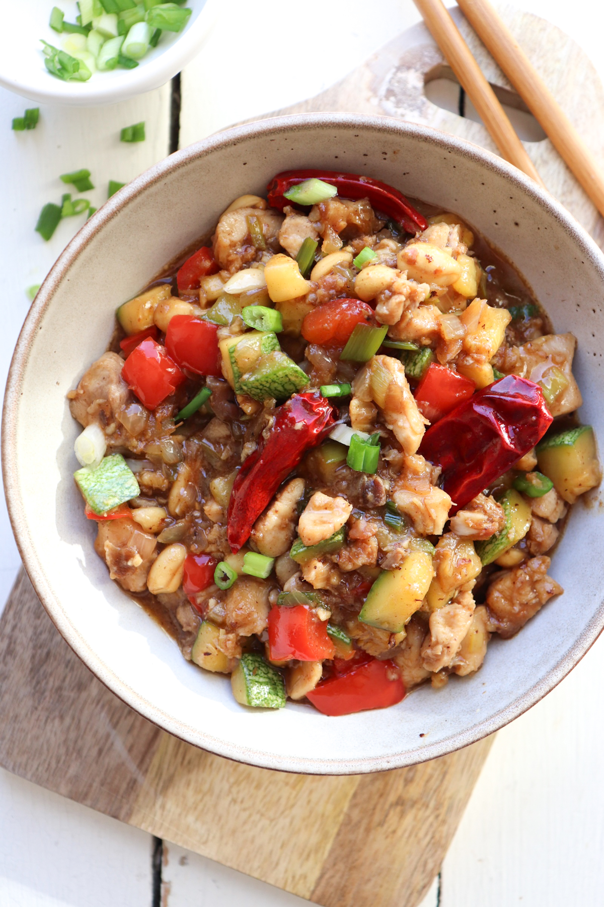bowl of kung pao chicken with green onions scattered around.