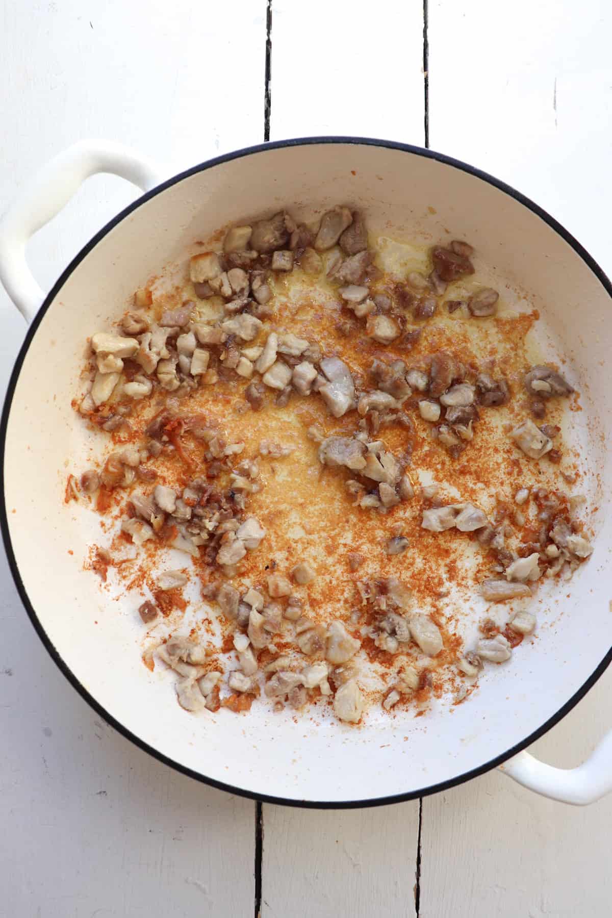 chicken pieces browning in a large white skillet.