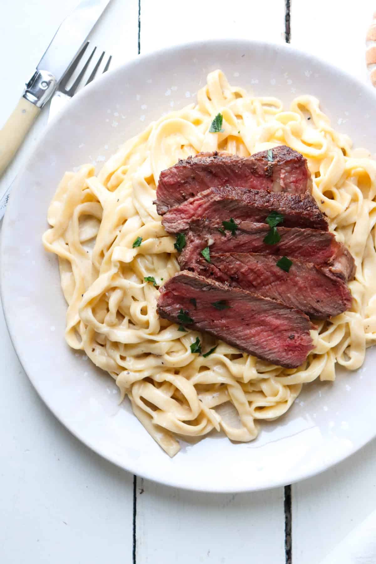 medium rare steak on fettuccine alfredo.