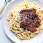 steak fettuccine alfredo topped with cheese.