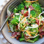 bowl of broccoli salad topped with cheese and bacon.
