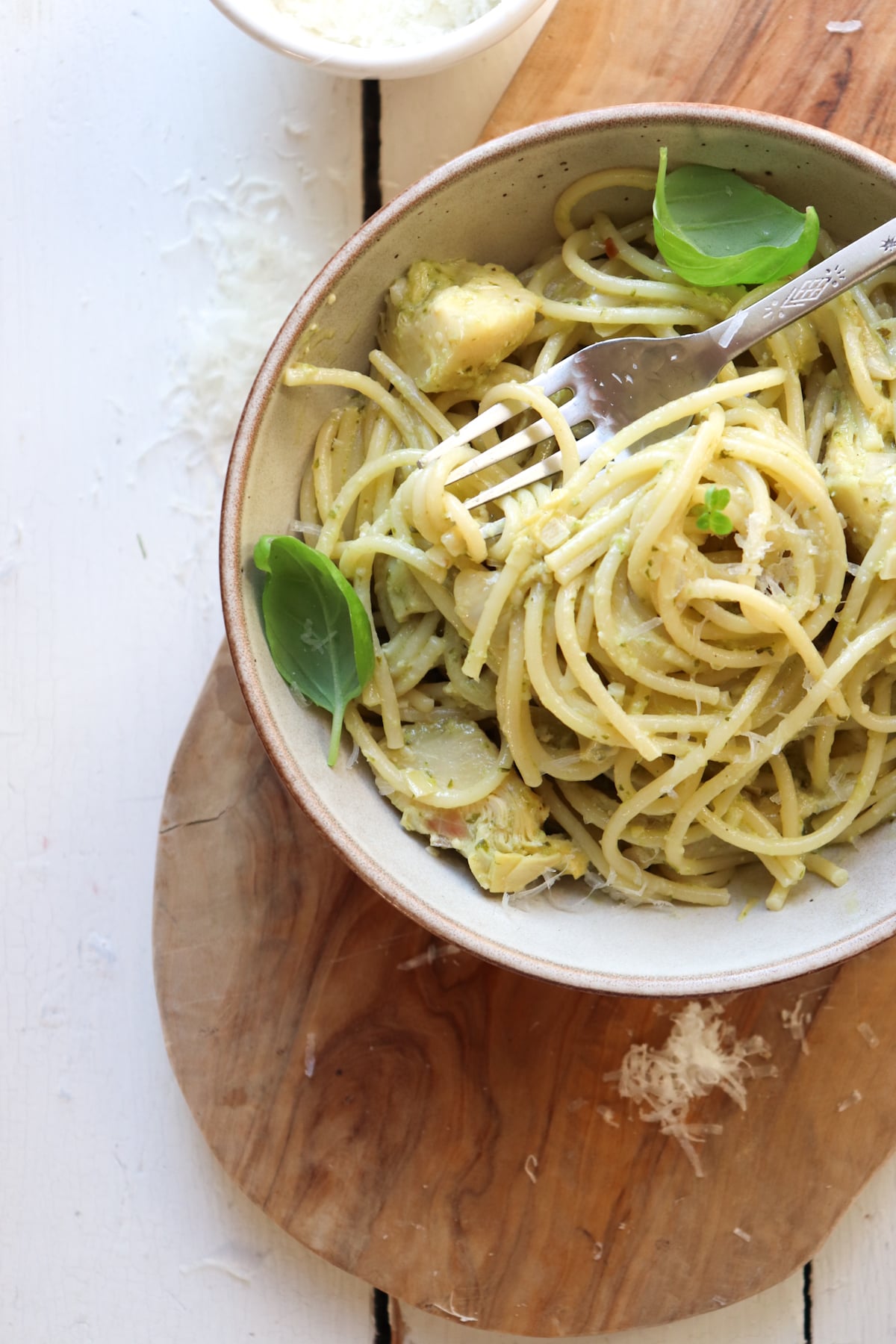 bowl of pesto artichoke pasta garnished with basil leaves with a fork in the bowl.