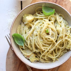 bowl of pesto artichoke pasta garnished with basil leaves.