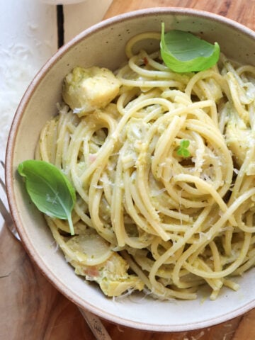 bowl of pesto artichoke pasta garnished with basil leaves.
