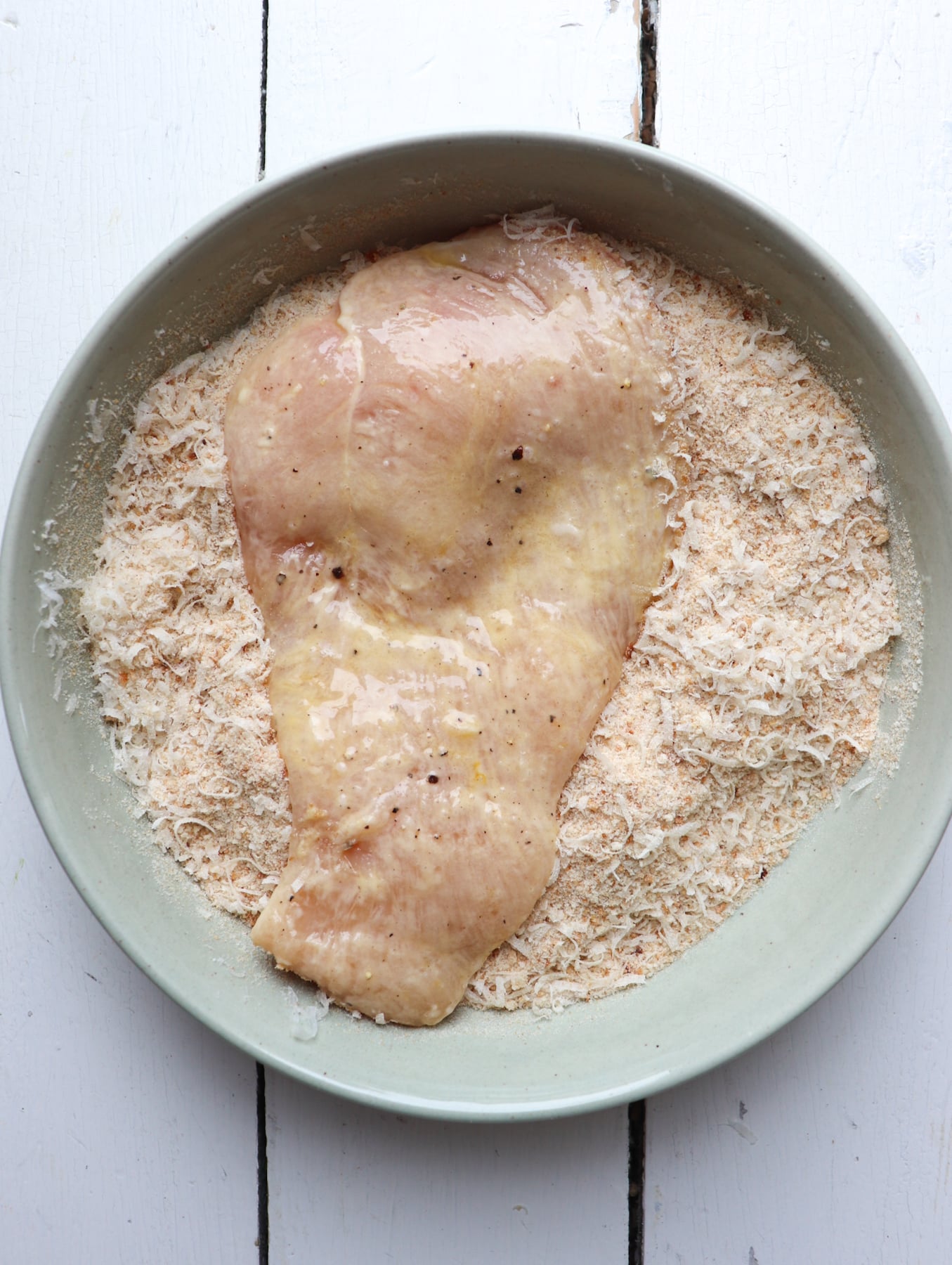 chicken after it has been coated in egg wash placed in bowl of breadcrumbs.