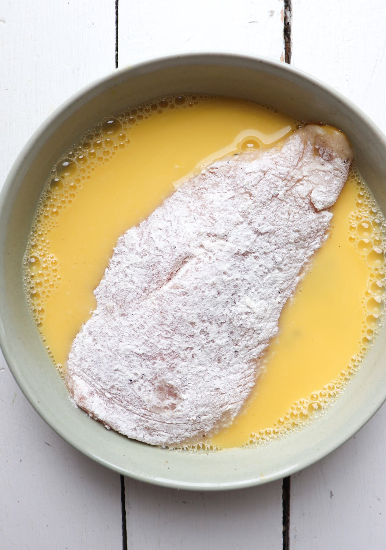 flour coated chicken cutlet being dipped in egg wash.