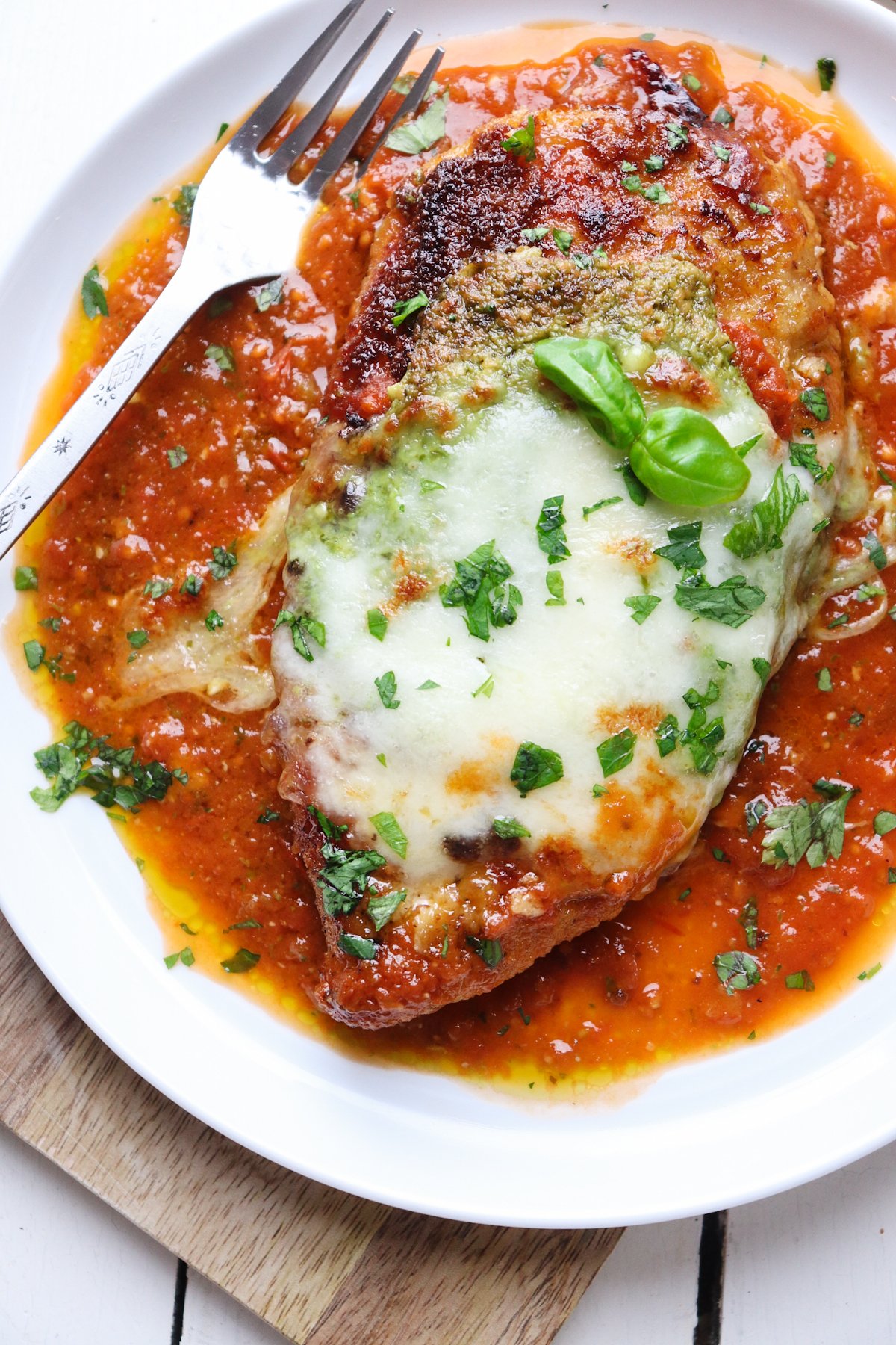 finished pesto chicken parmesan piece on a bed of marinara sauce with a fork on the plate.