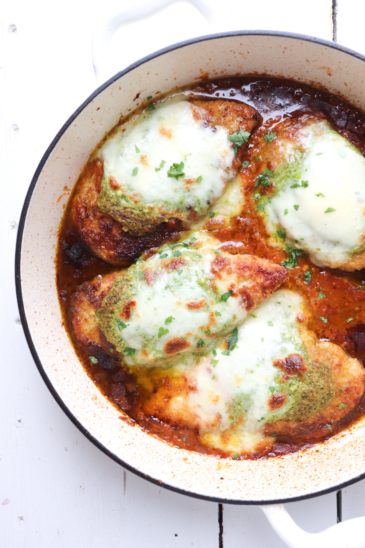 finished chicken pesto parmesan on white cast iron skillet.