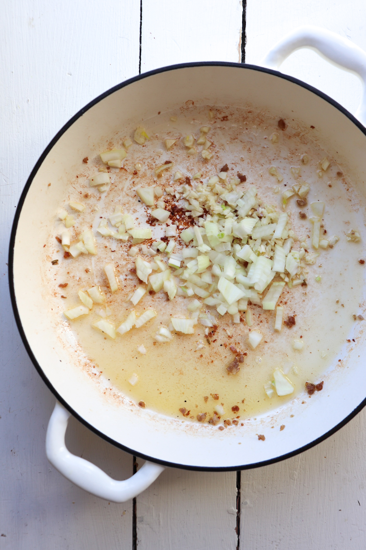 onions and garlic sauteing in a white dutch oven.