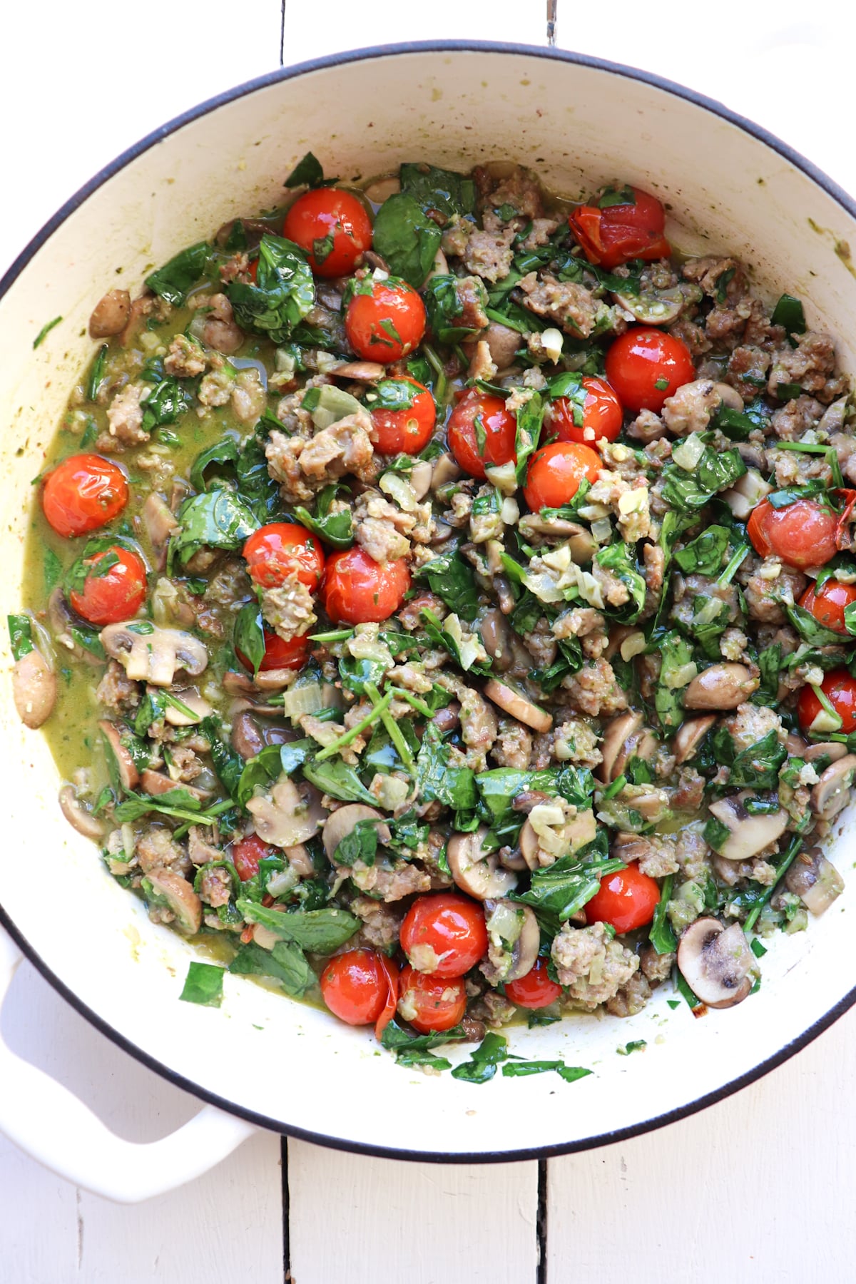 sausage, tomatoes, and spinach cooking in a pot.