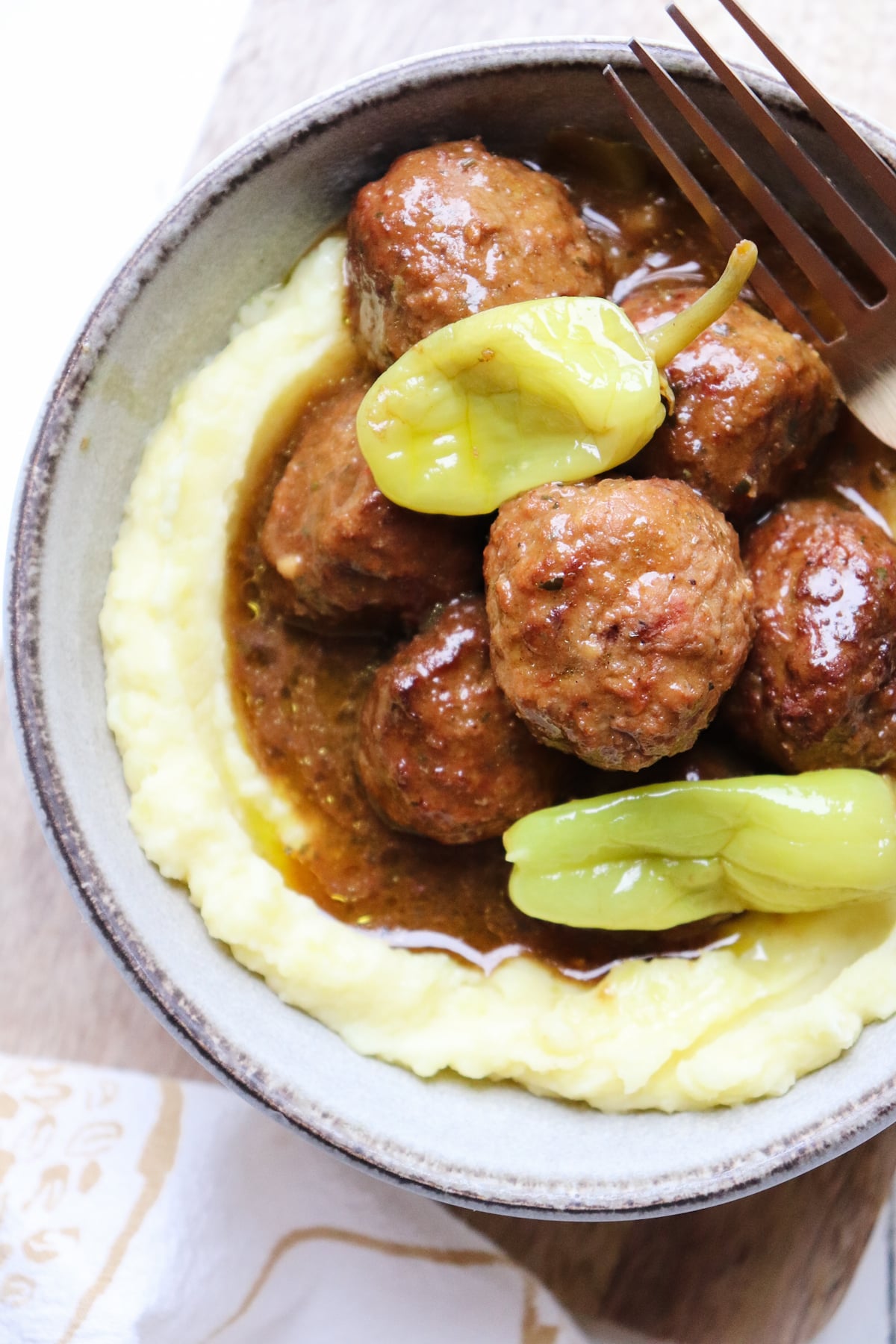 bowl of mississippi meatballs on a bed of mashed potatoes with a fork to the side.