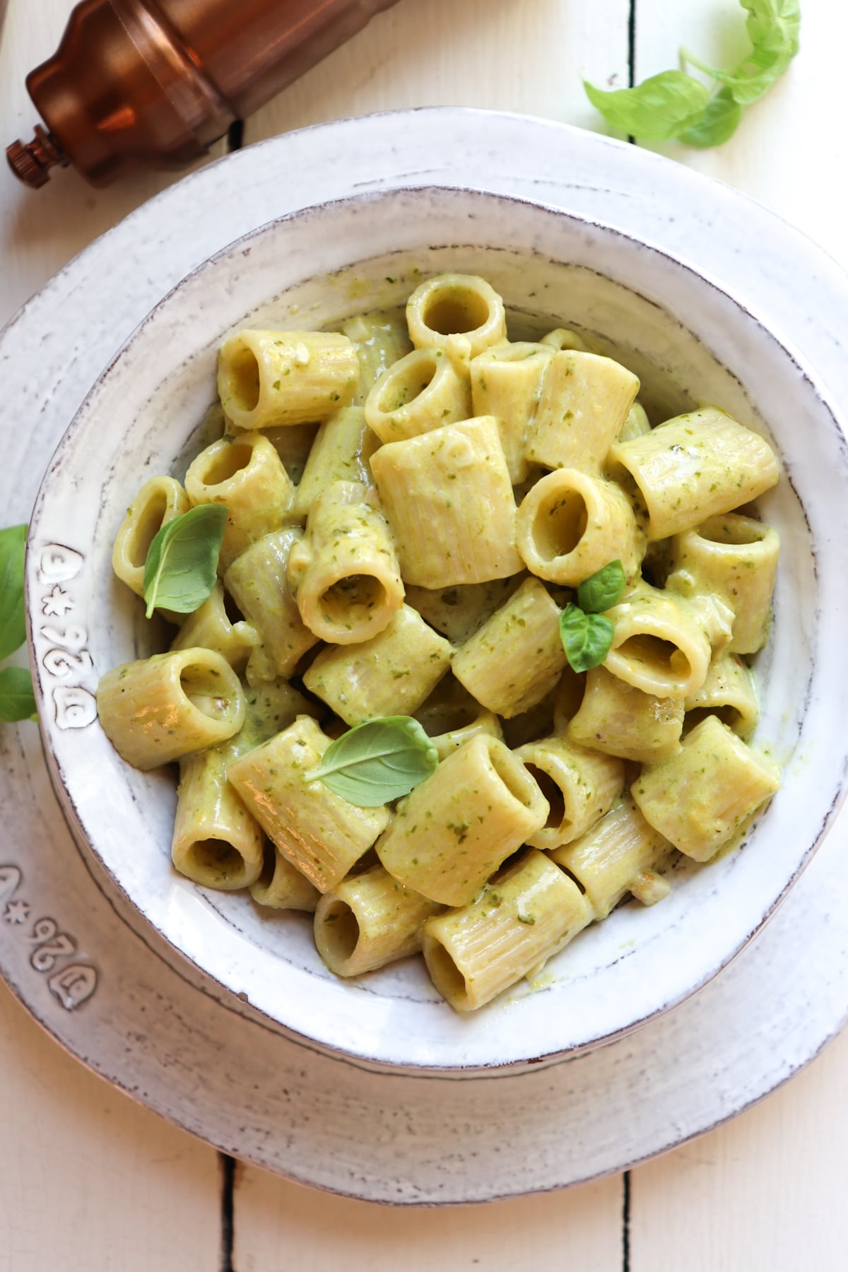 bowl of creamy garlic pesto pasta garnished with basil leaves with pepper shaker in the background.