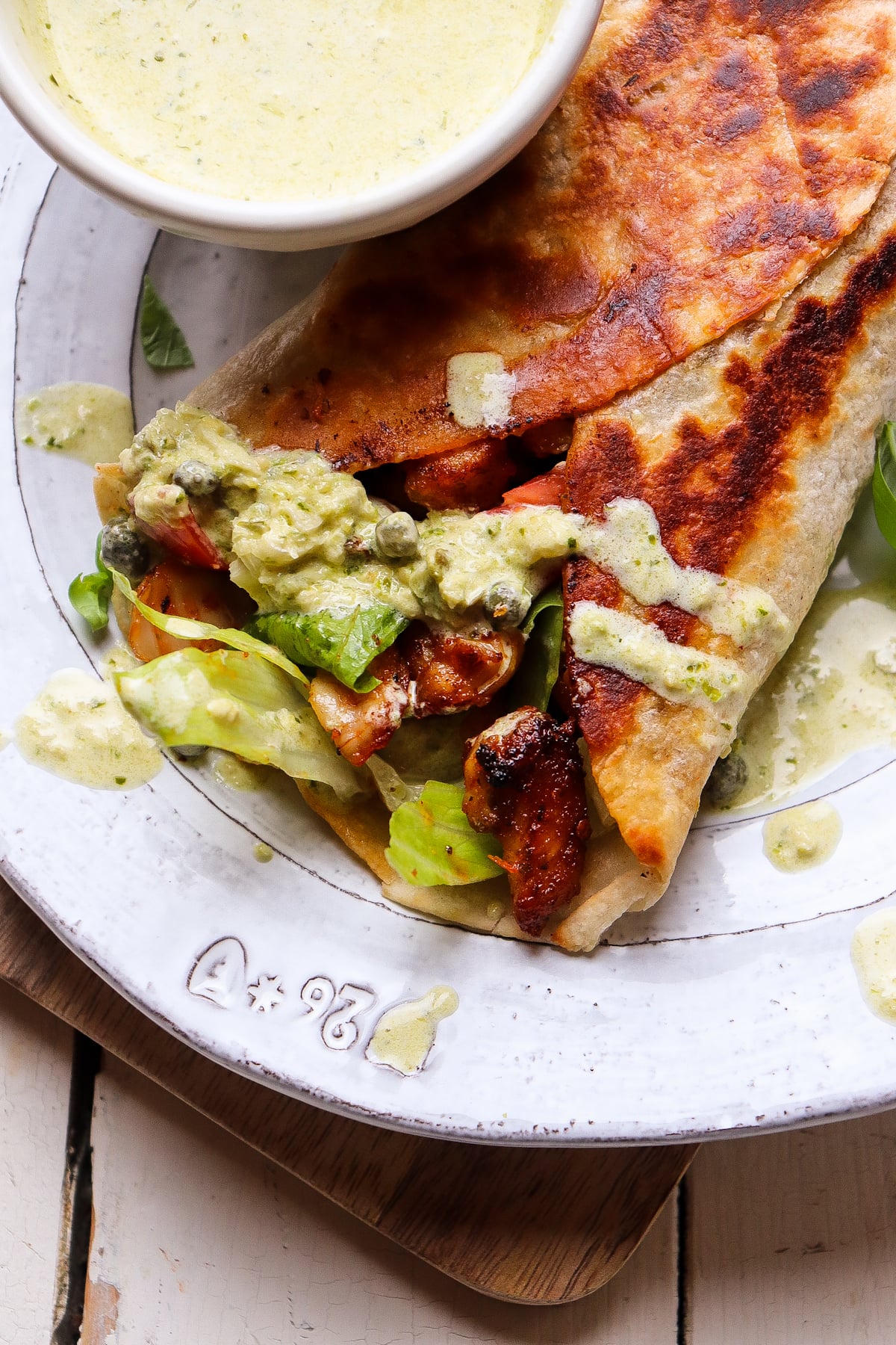 one pesto chicken wrap on a plate with extra sauce.