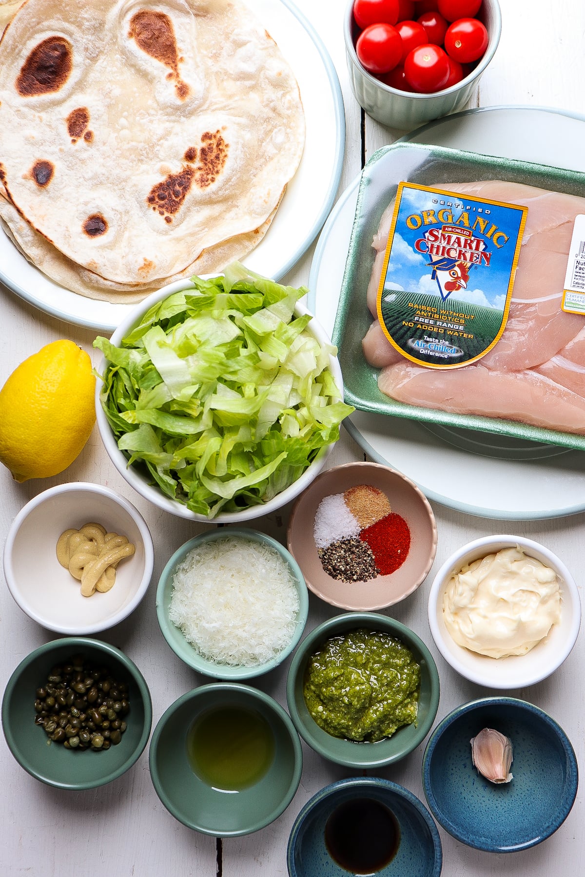 ingredients for pesto chicken wraps on a white table.