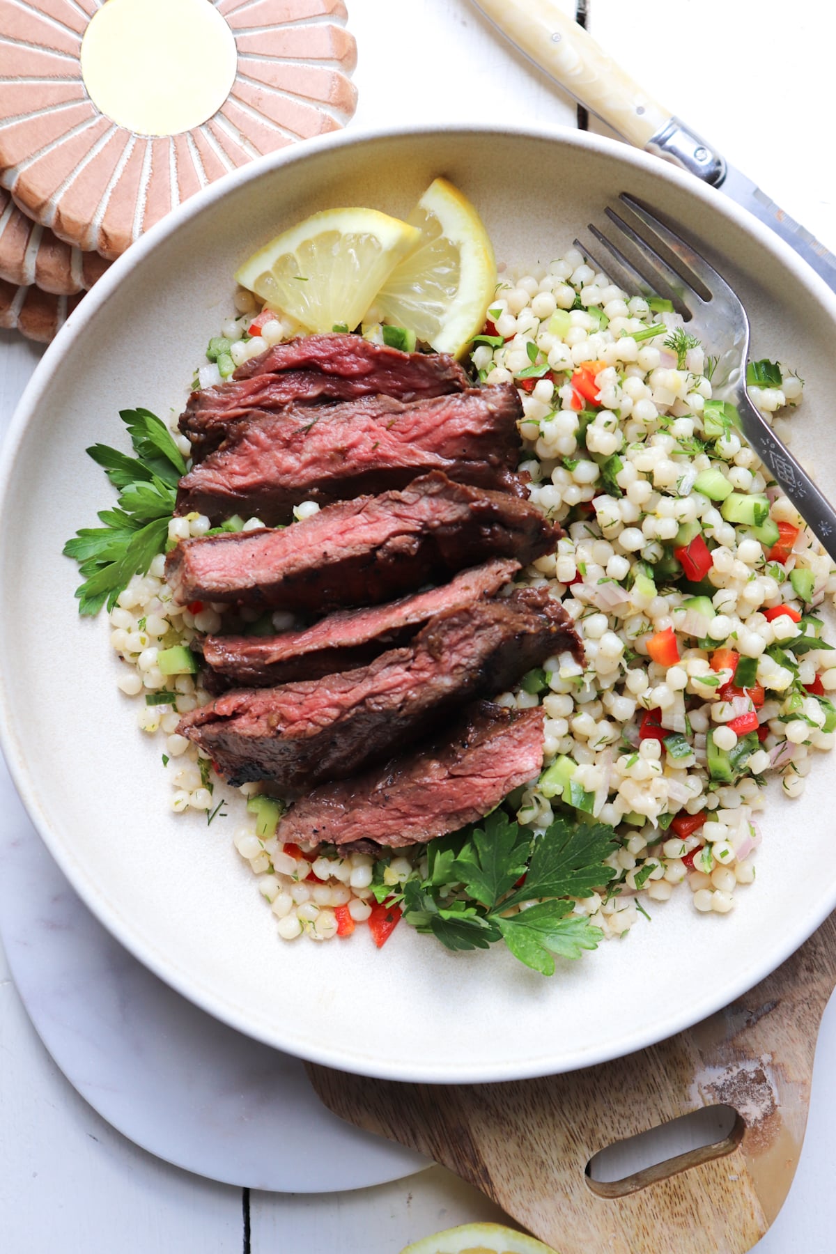 skirt steak laid on top of an couscous salad and garnished with lemon and parsley.
