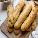 pile of garlic butter sourdough breadsticks on a wooden cutting board.