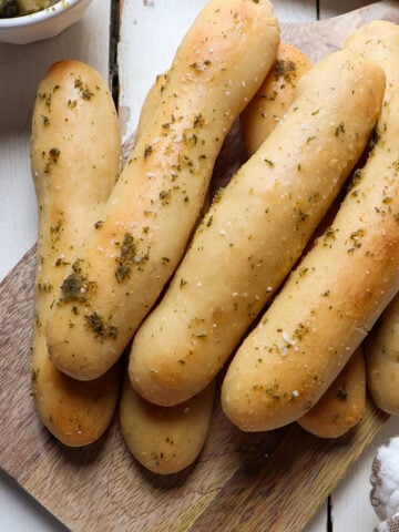 pile of garlic butter sourdough breadsticks on a wooden cutting board.