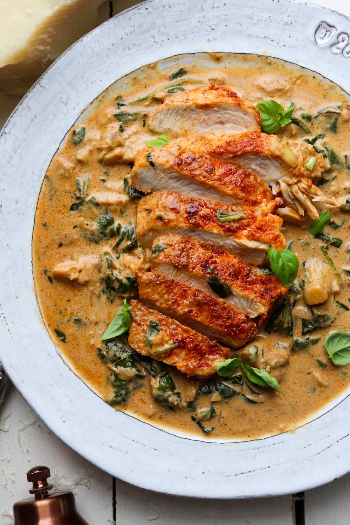 sliced chicken breasts on a bed of spinach artichoke sauce garnished with basil.