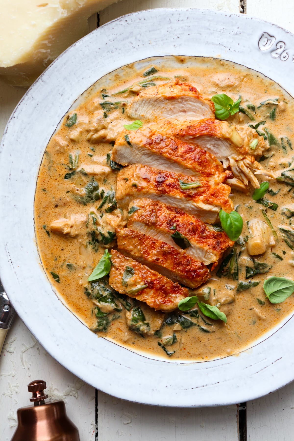 sliced chicken breasts on a bed of spinach artichoke sauce garnished with basil.