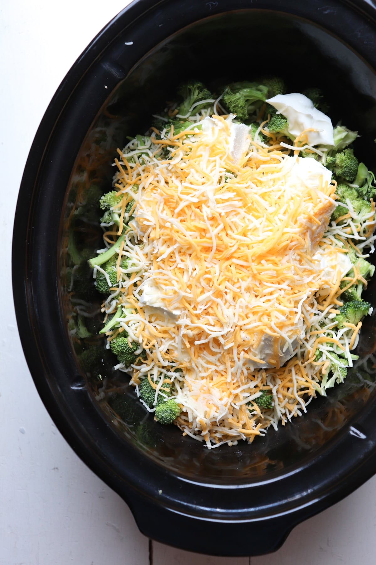 cheese sprinkled on Greek yogurt and broccoli in crock pot.
