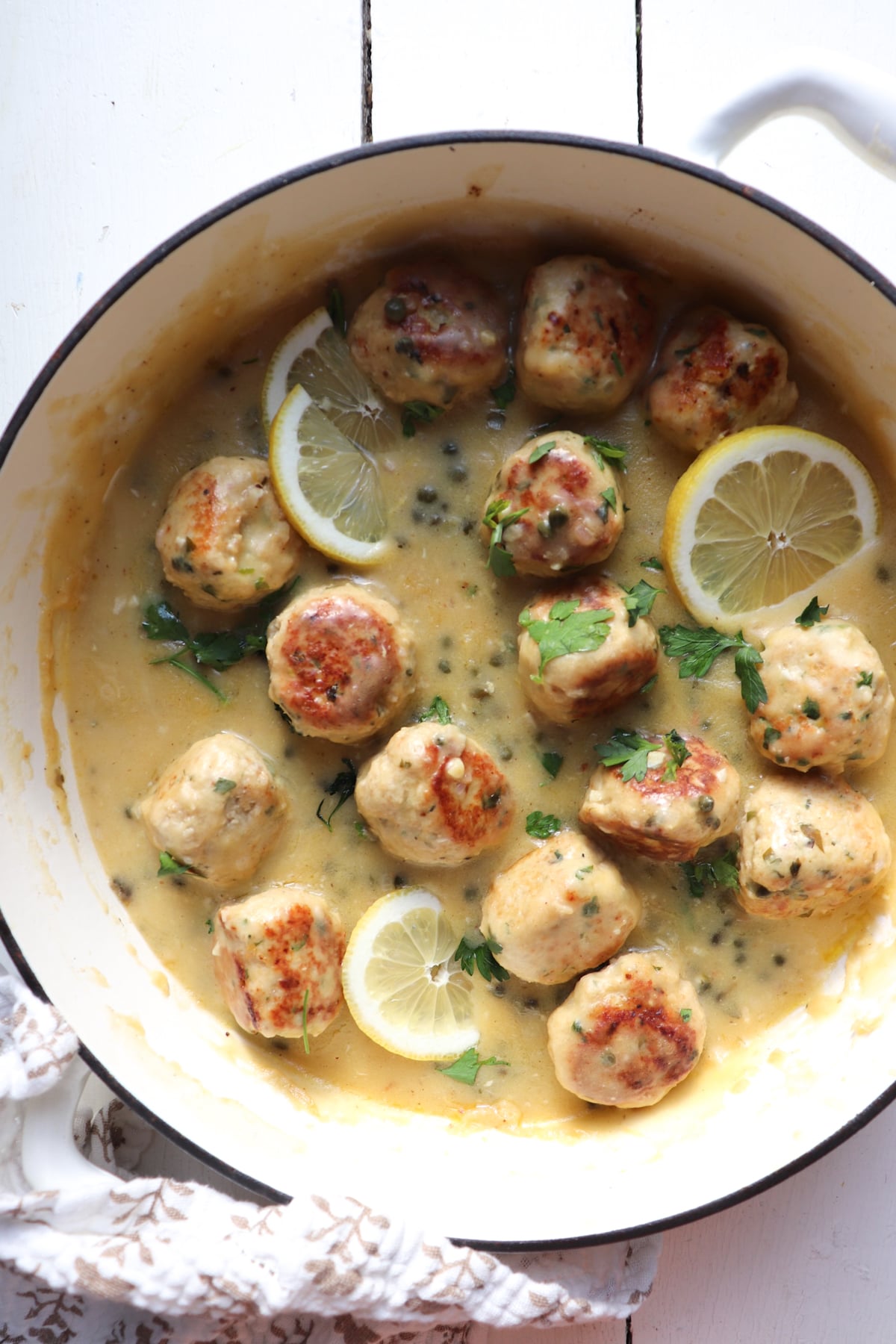 finished chicken piccata meatballs in sauce in a white skillet.