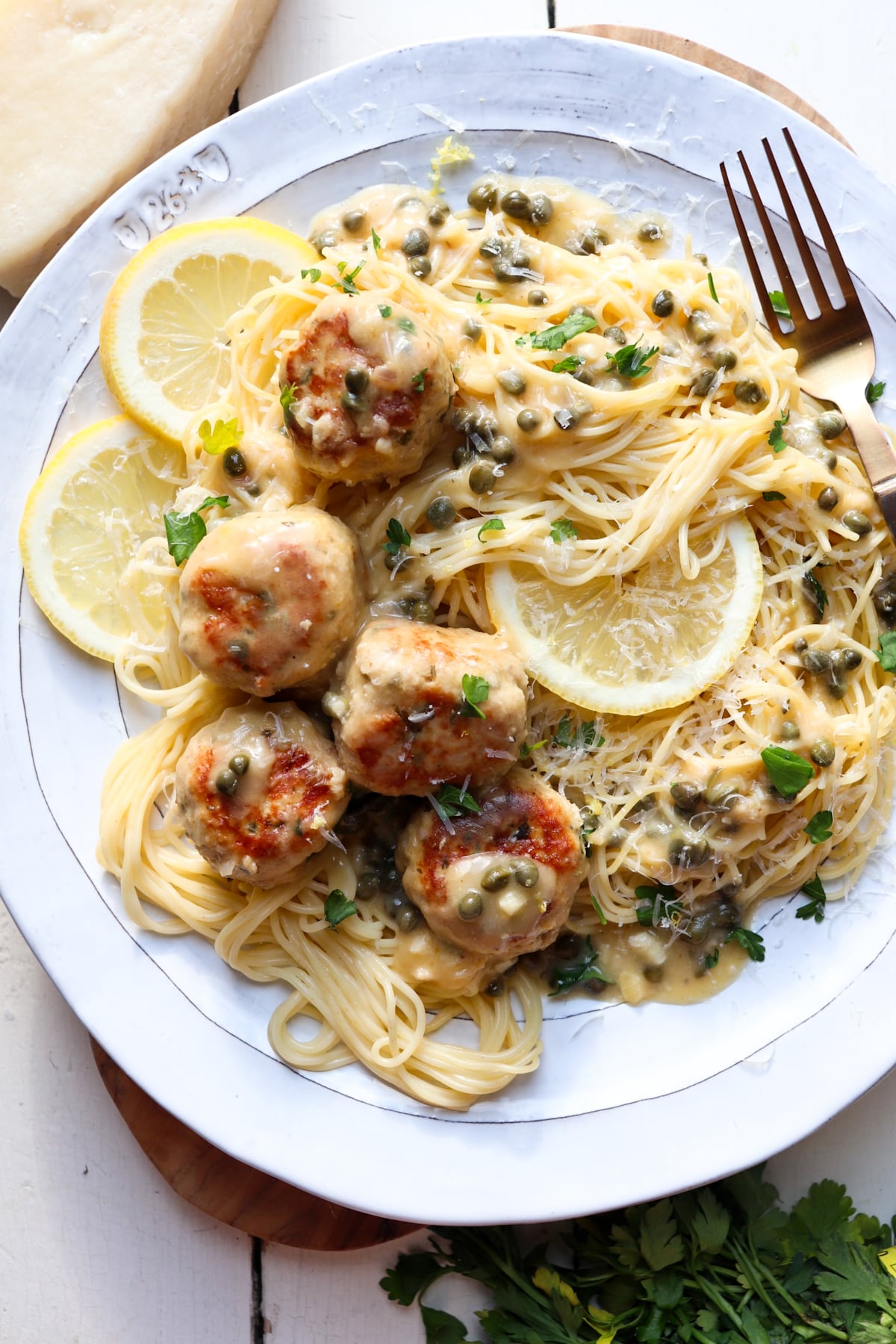 plate of chicken piccata meatballs with sauce on a plate of angel hair pasta.