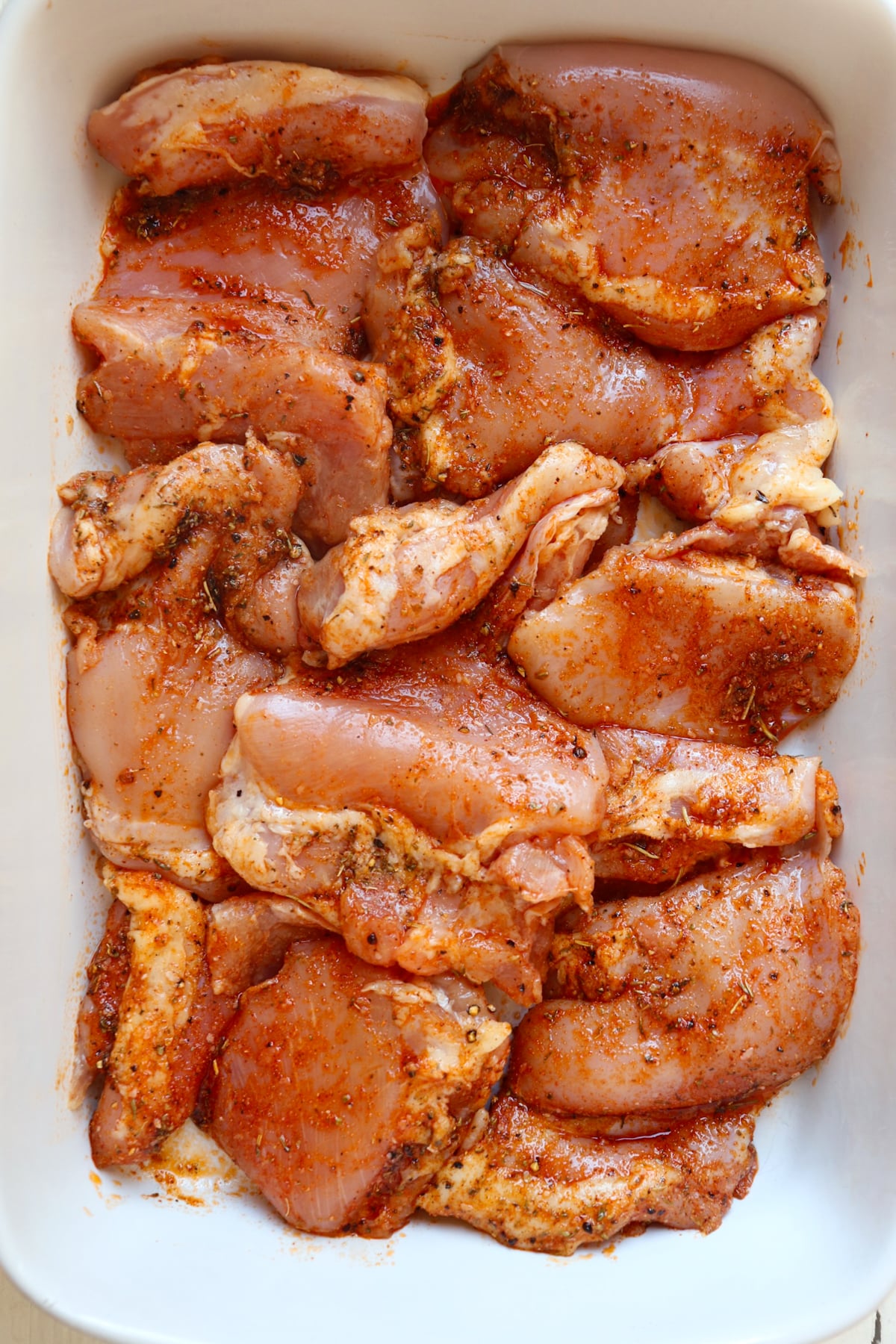 seasoned chicken thighs uncooked in a white baking dish.