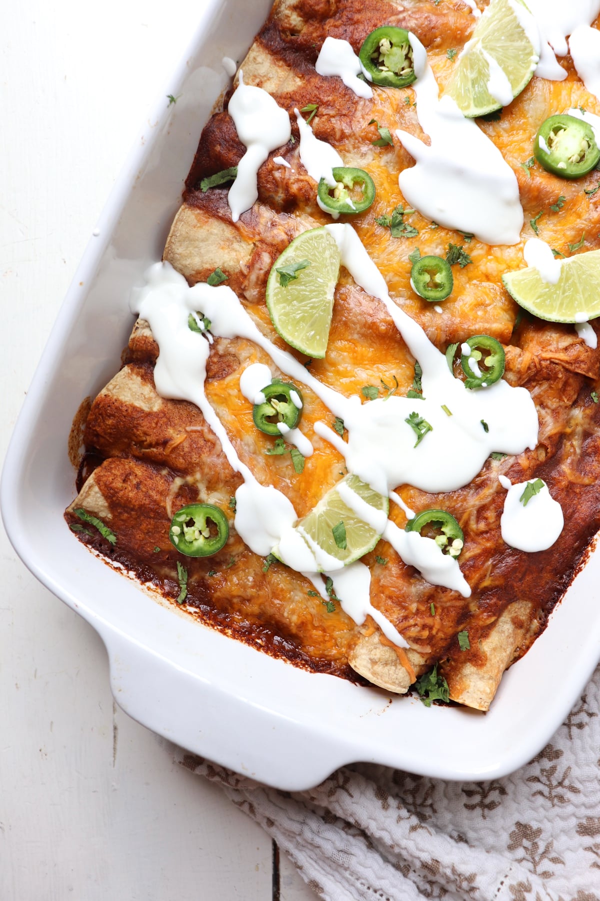 finished dish of enchiladas topped with sour cream, jalapenos, and limes.
