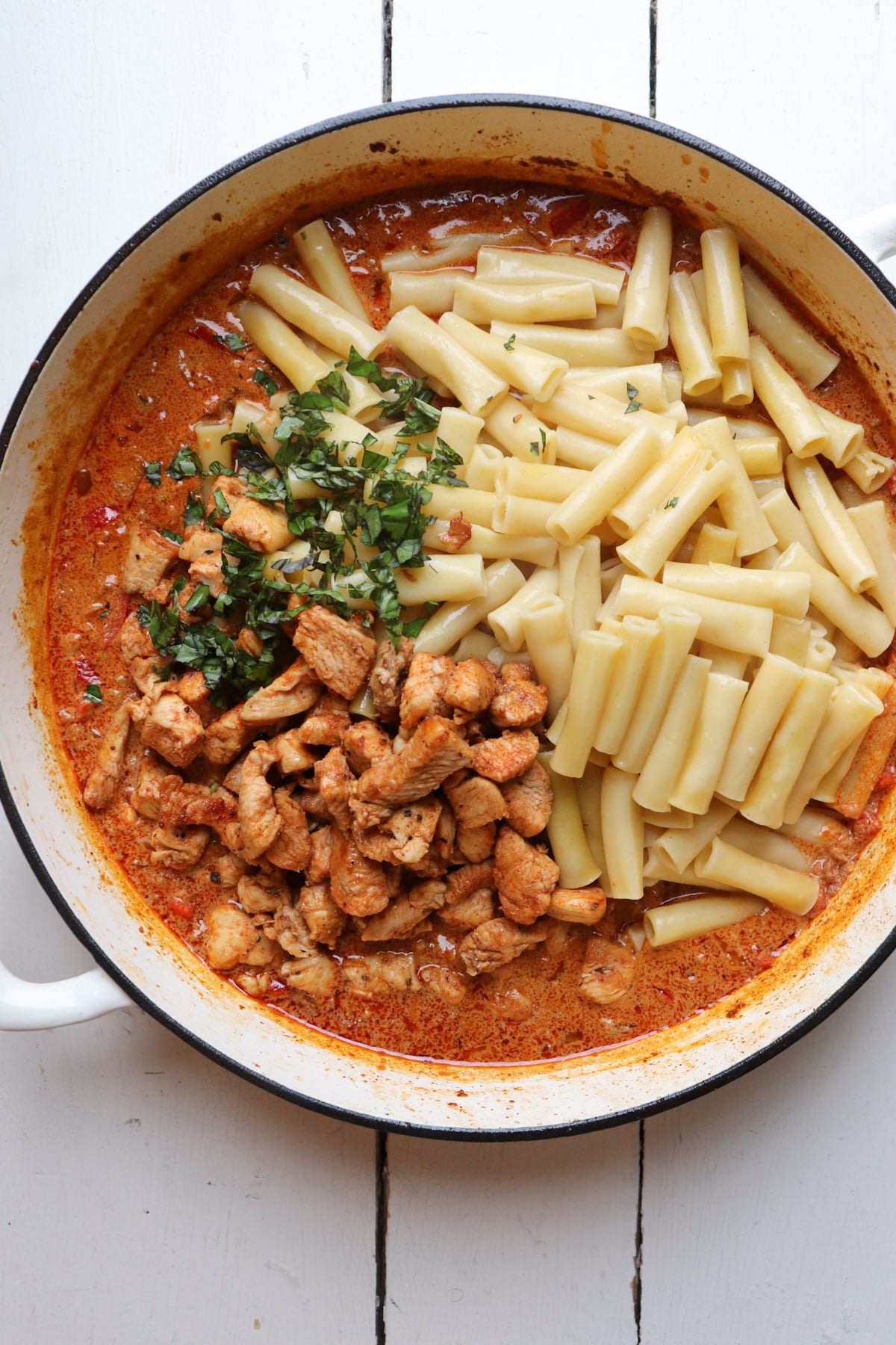 pasta, basil, and chicken added to cream sauce in pan.