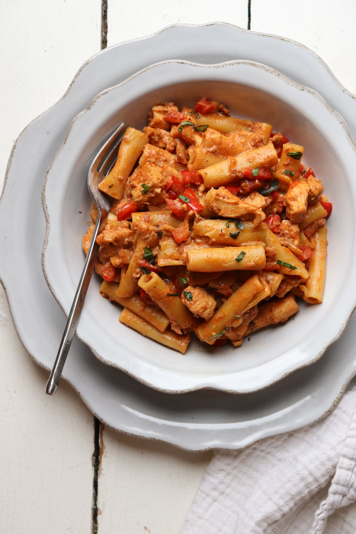 creamy chorizo pasta with chicken pieces in a white bowl with a fork.