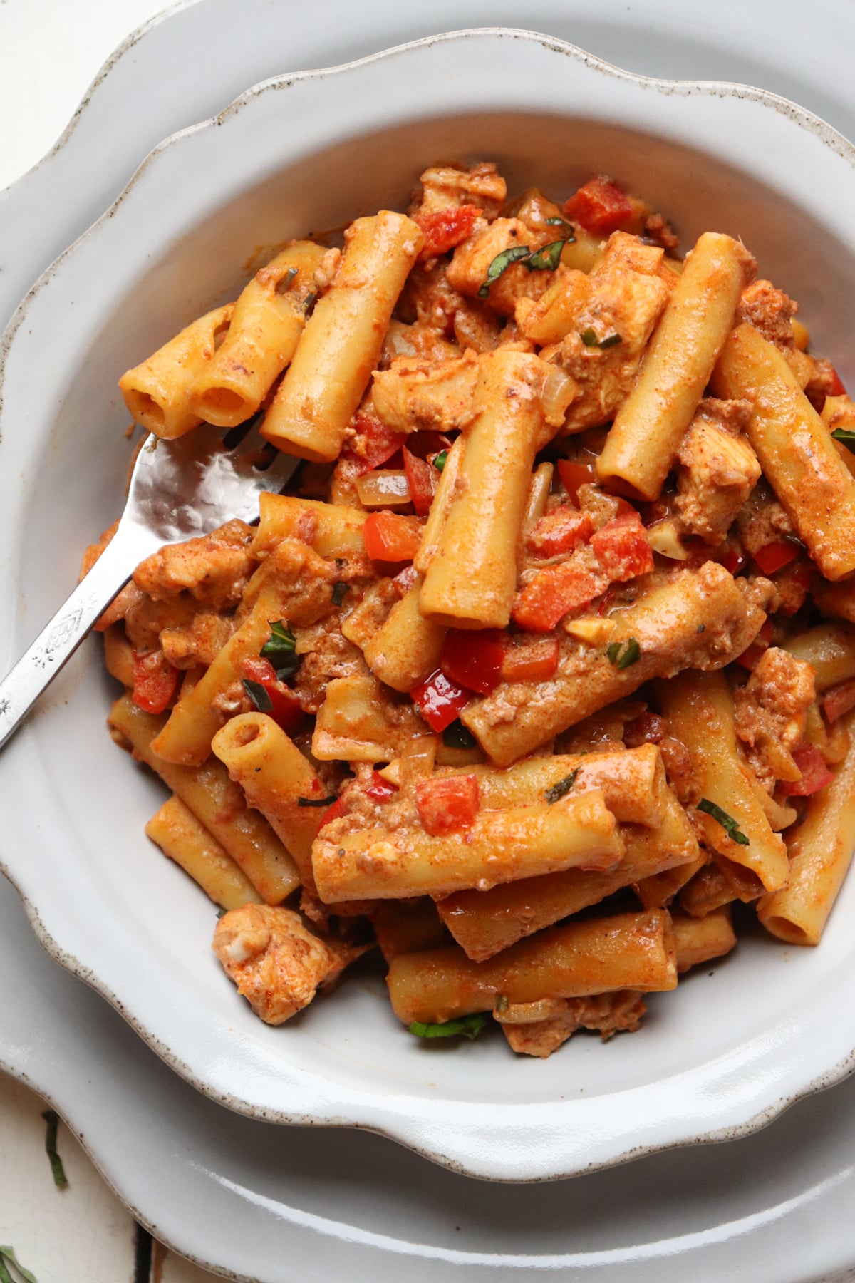 creamy chorizo pasta with chicken pieces in a white bowl with a fork.