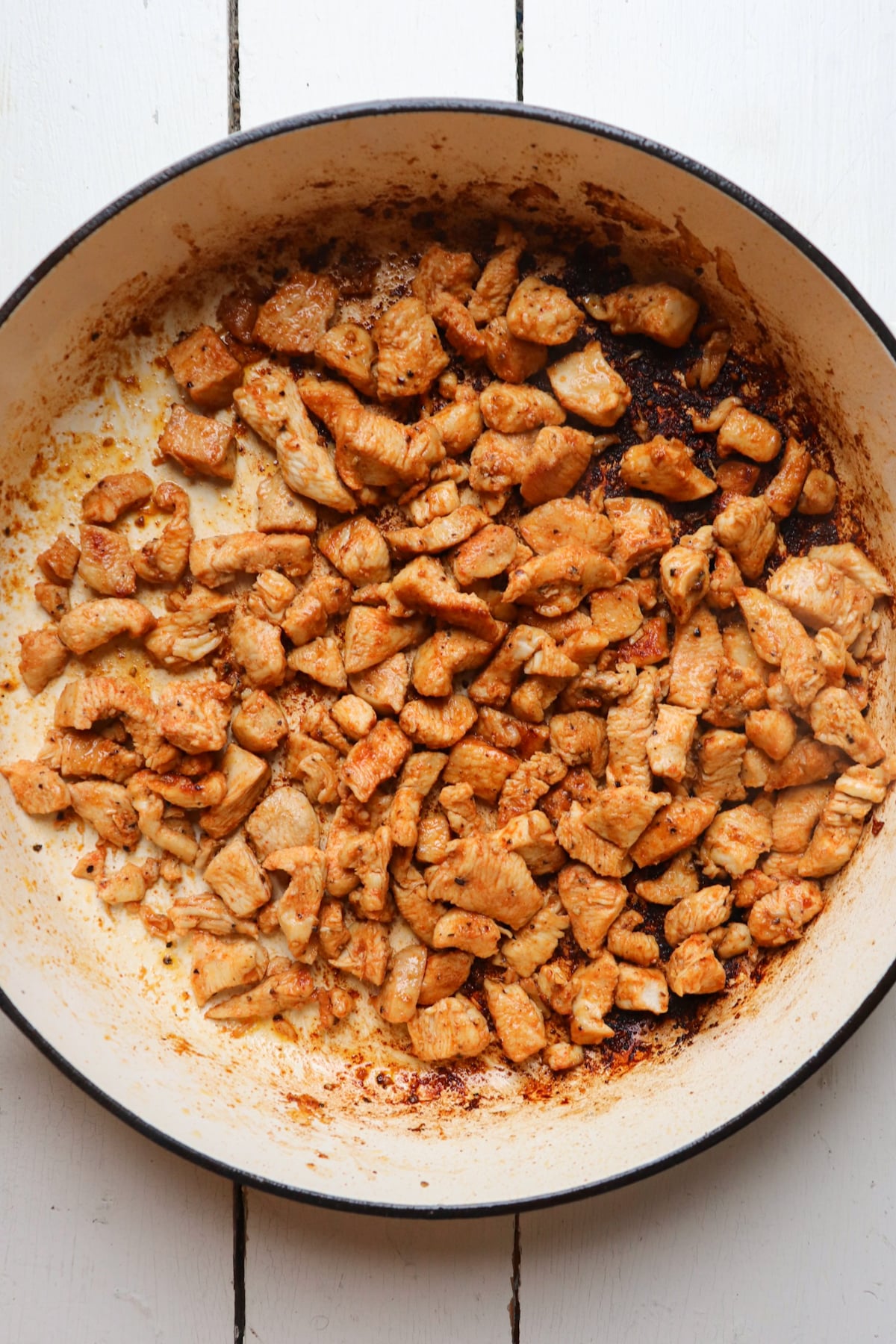 chicken pieces cooking in white skillet.