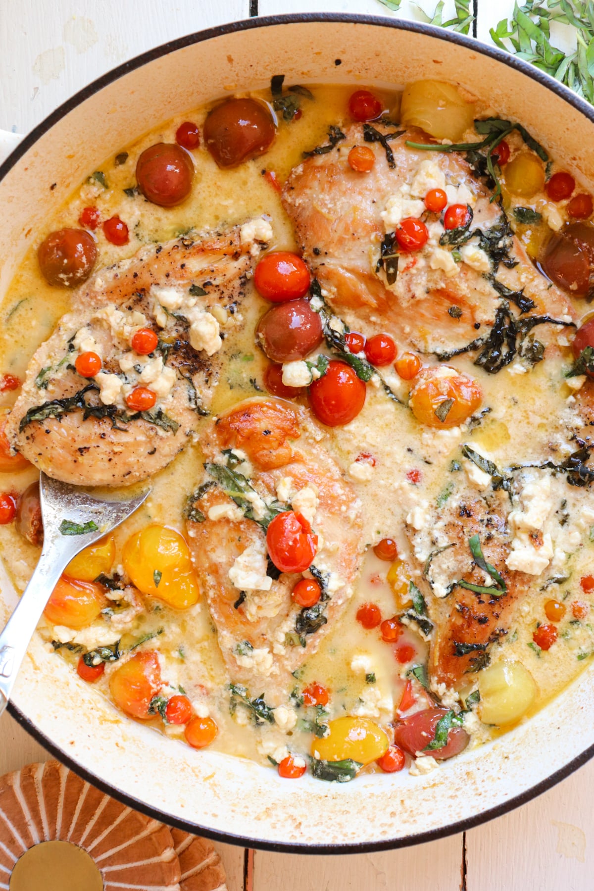 finished chicken feta bake shown in white dutch oven with a serving spoon.