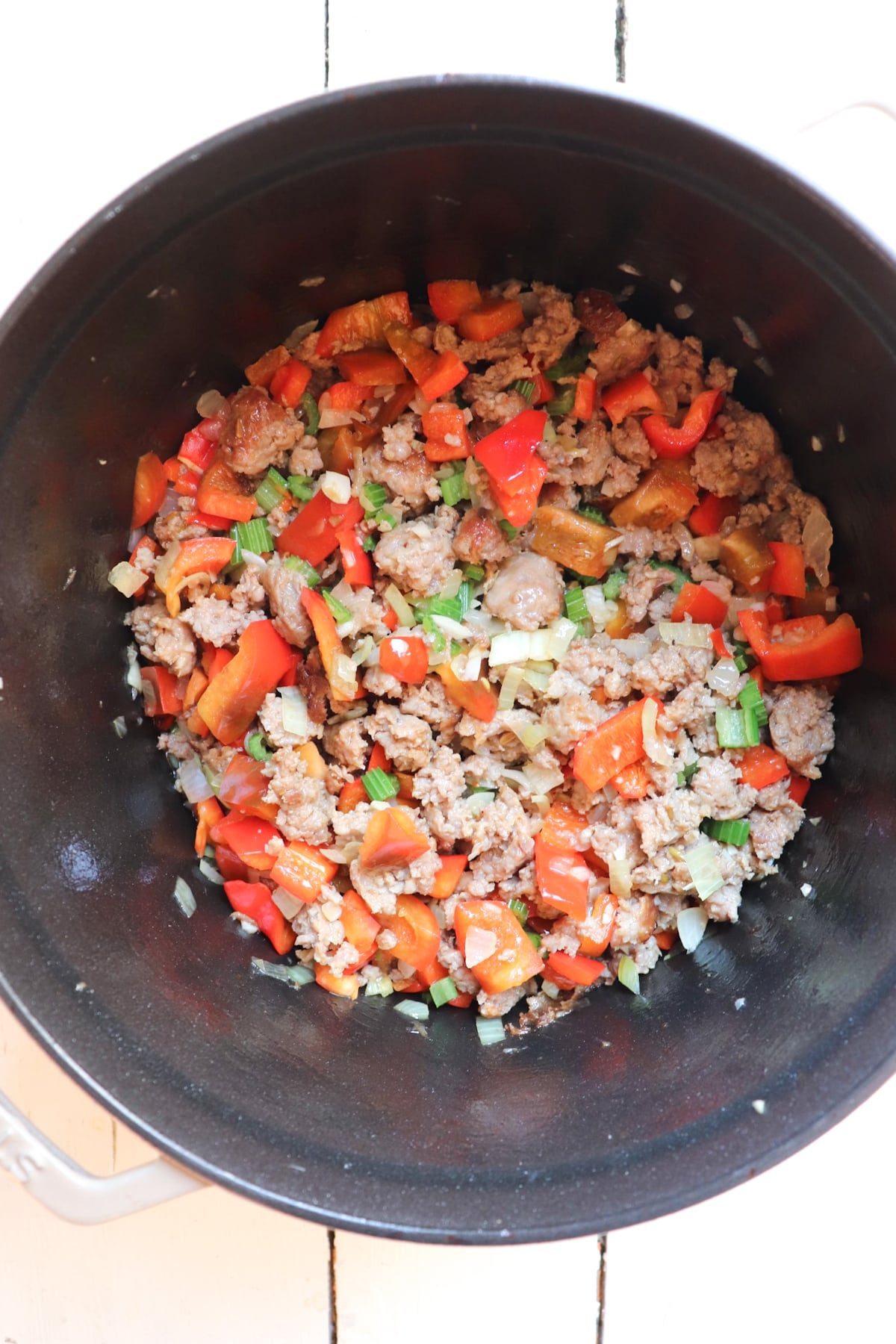 red bell pepper added to sausage in pot.