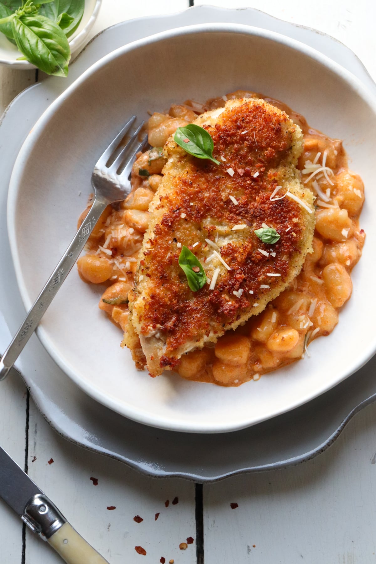crispy chicken cutlets on vodka sauce gnocchi garnished with basil and fork.